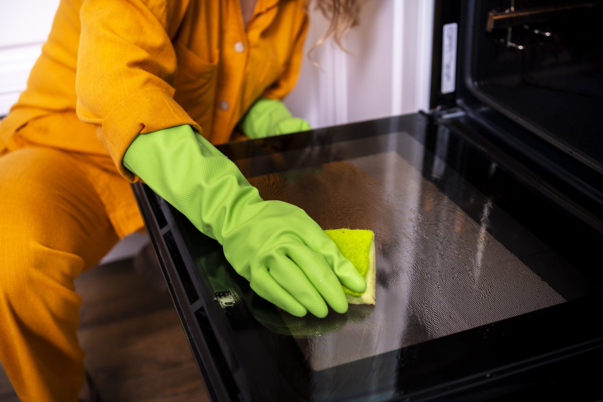 Schoonmaker met groene handschoenen reinigt de glazen deur van een oven